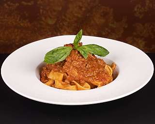 Piatto di pasta con ragù di carne e foglie di basilico fresco.