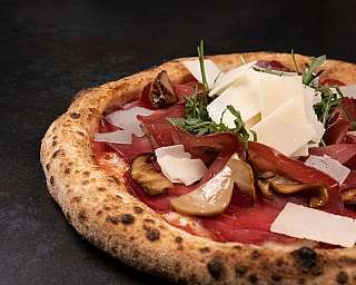 Pizza con prosciutto, funghi e scaglie di formaggio.
