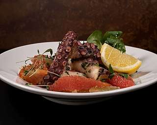 Ein Teller mit gegrilltem Oktopus und frischen Zitrusfrüchten.